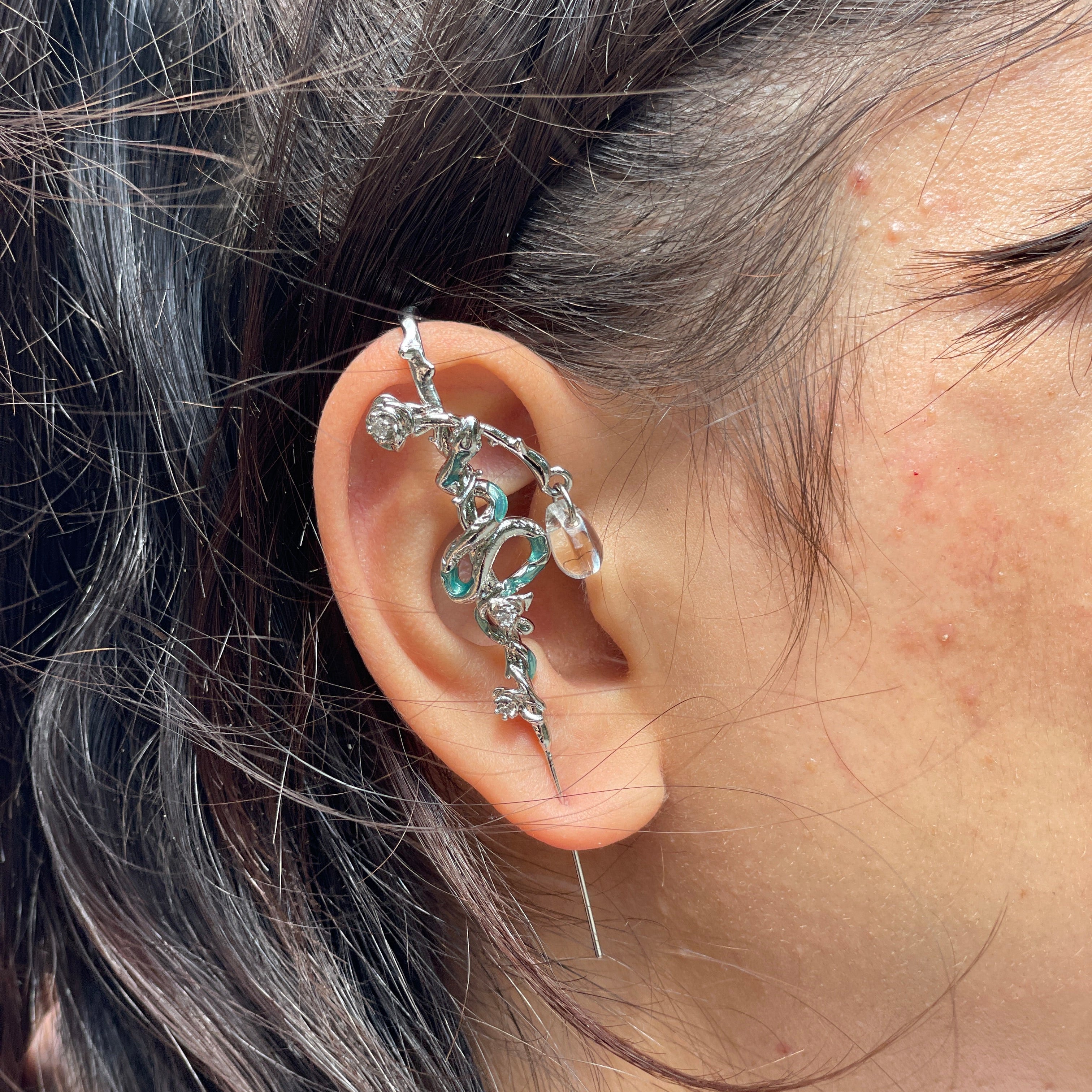 Close-up of an ear with a decorative silver earring against a neutral background