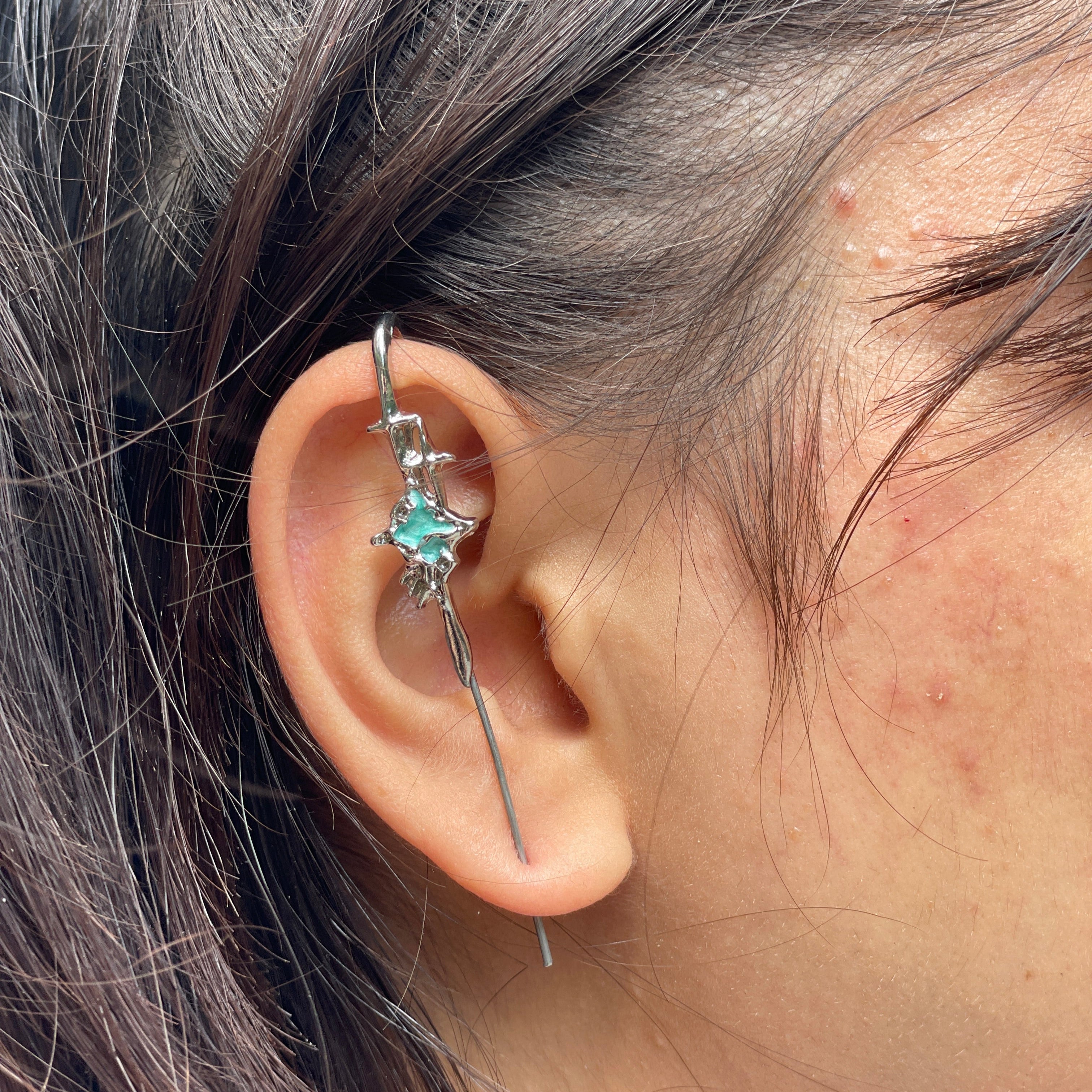 Close-up of an ear with a silver earring featuring a green gemstone.
