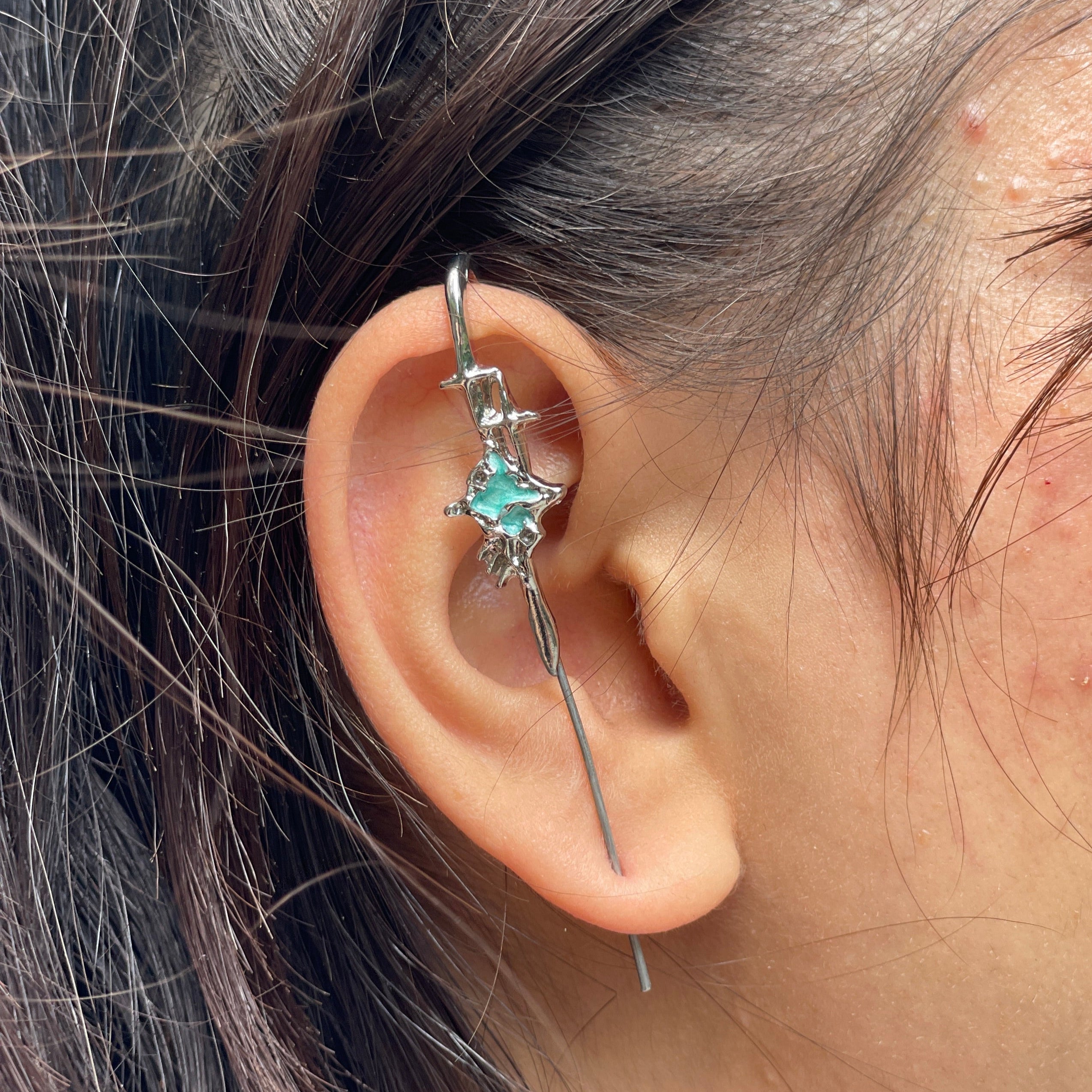 Close-up of an ear wearing a silver earring with a green gemstone, surrounded by hair.