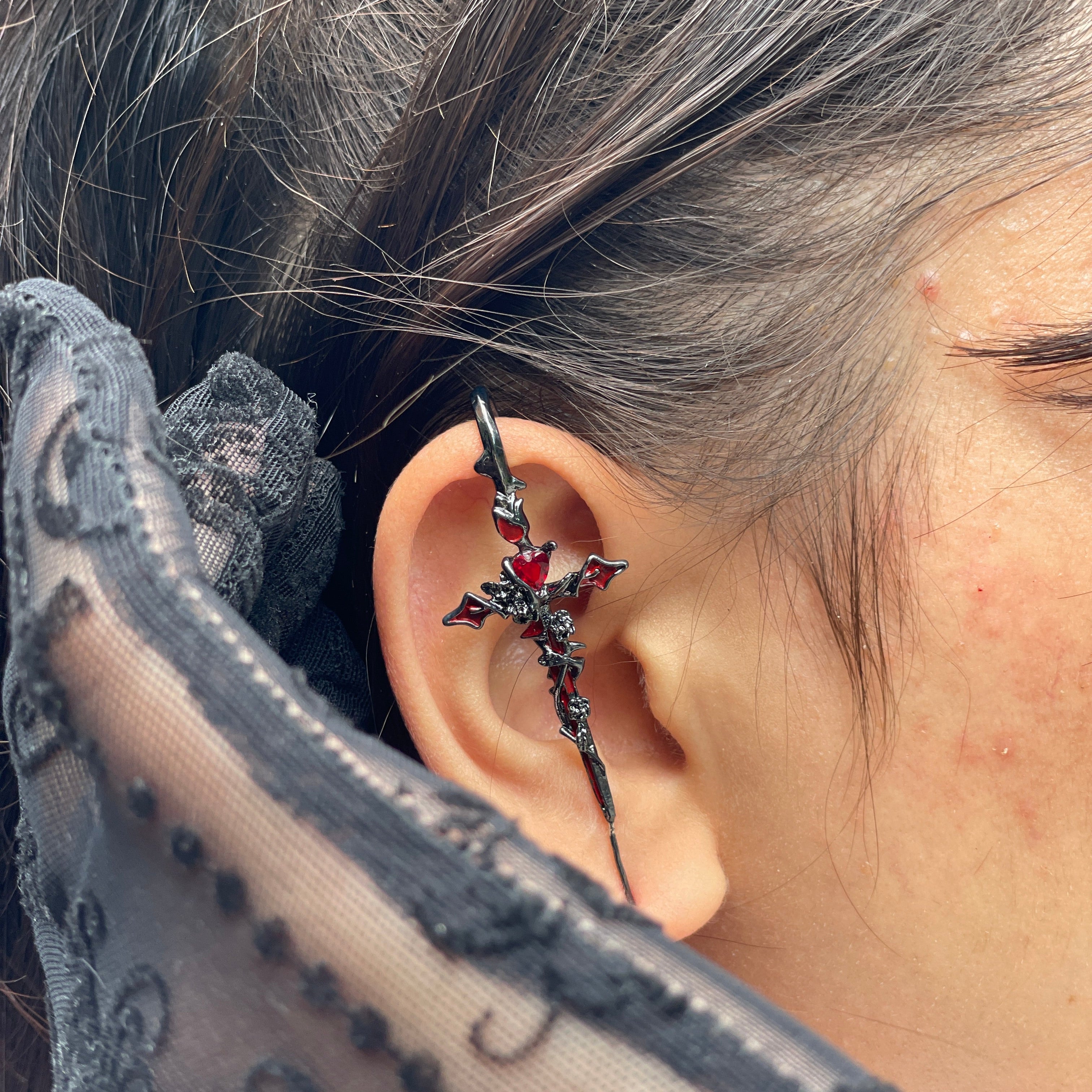 Close-up of an ear with a decorative earring, wearing a sheer black garment.
