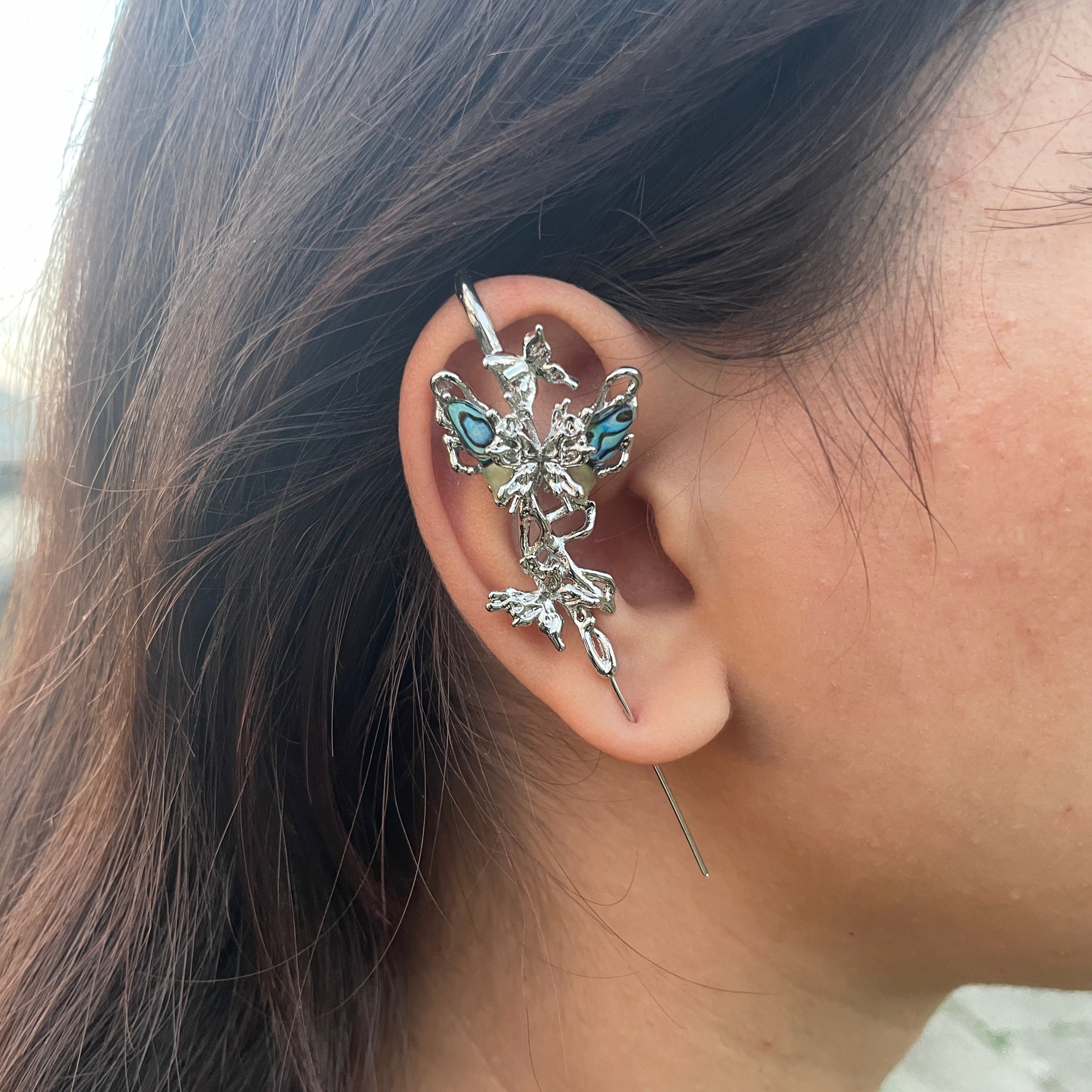 Close-up of an ear wearing a silver earring with blue gemstones, hair partially obscuring the view.