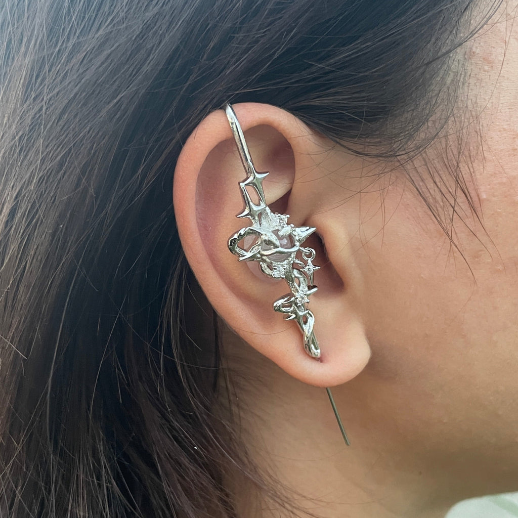 Close-up of an ear with a silver ear cuff featuring star designs.