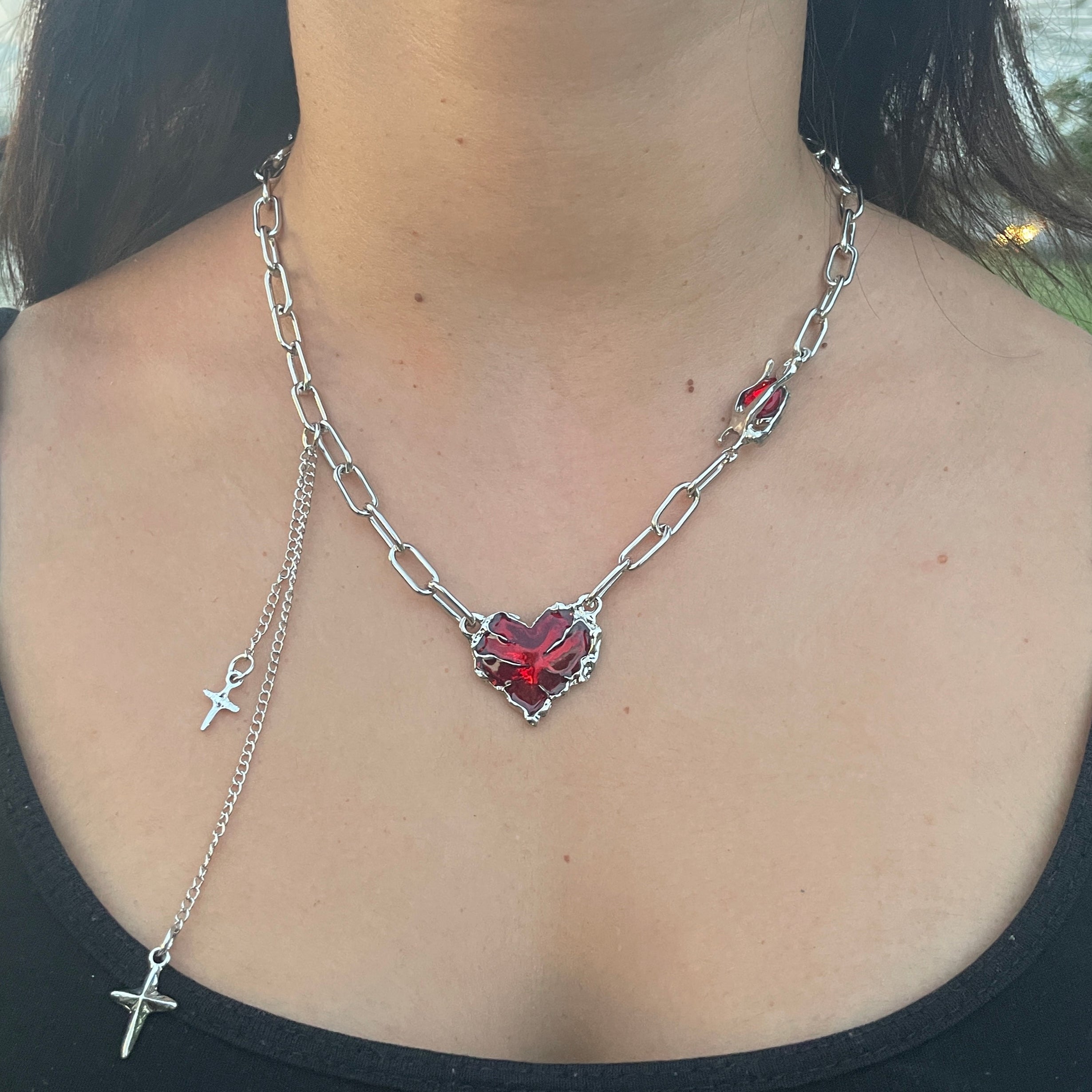 Person wearing a black top with a decorative chain and heart pendant on their shoulder.