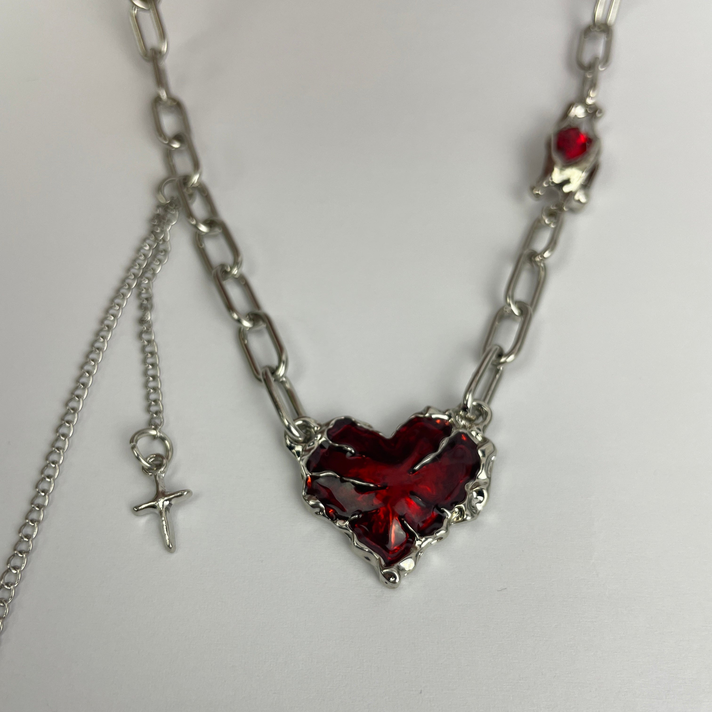 Silver chain necklace with red heart-shaped pendants on a white background