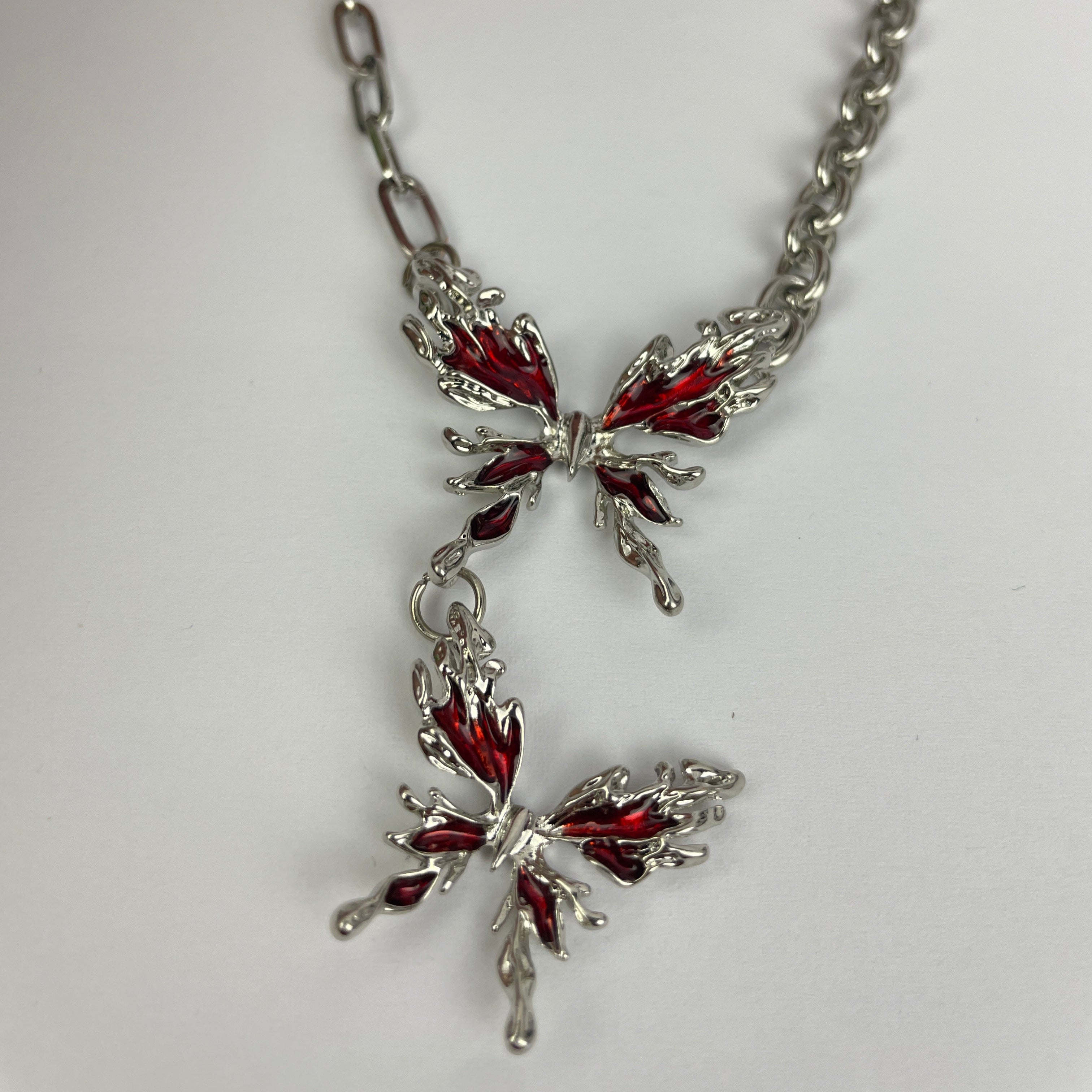 Butterfly-shaped jewelry piece with red accents on a chain against a white background